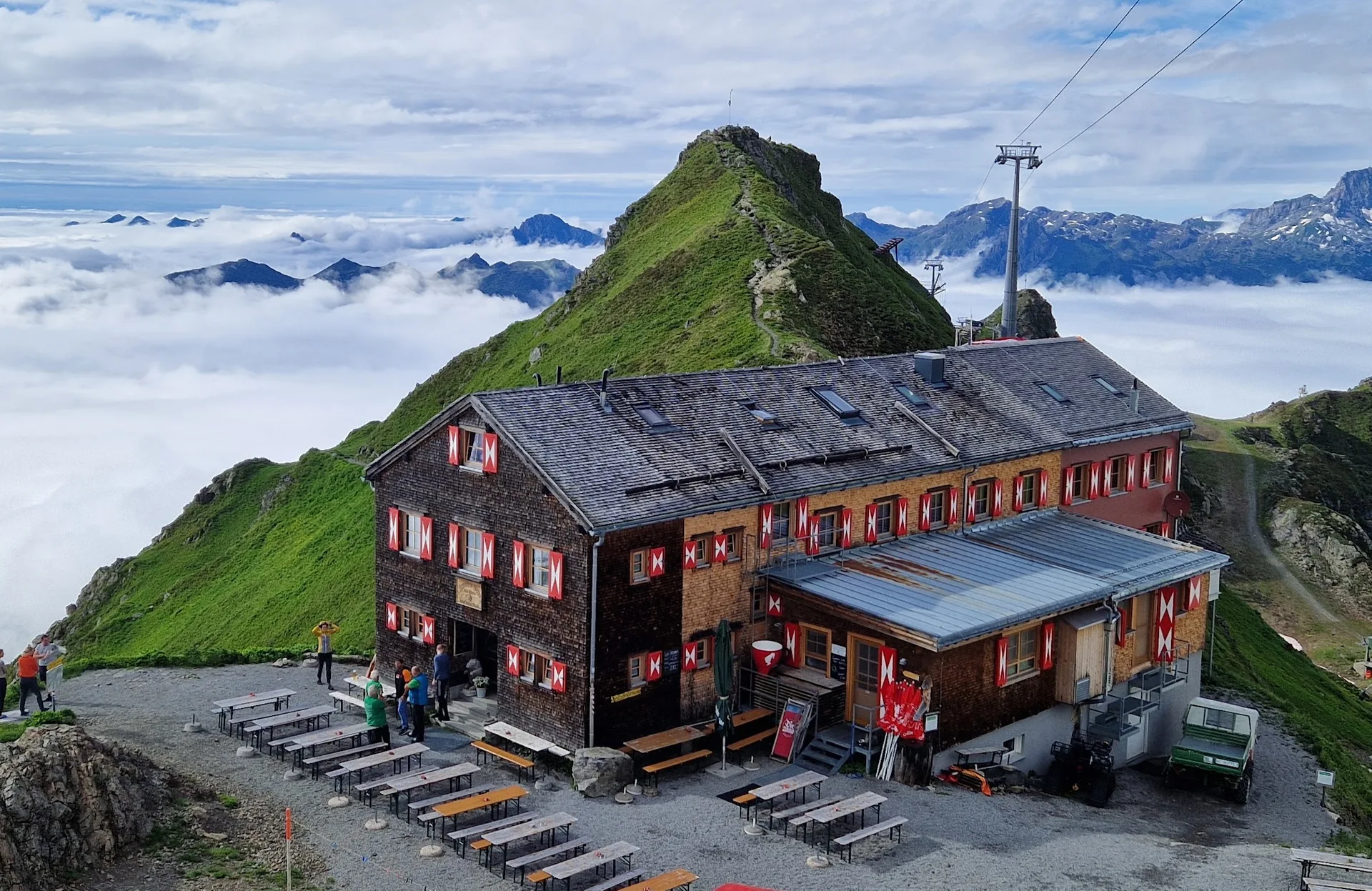 Die Wormser Hütte über einem Wolkenmeer, davor die Sonnenterrasse mit Bierbänken