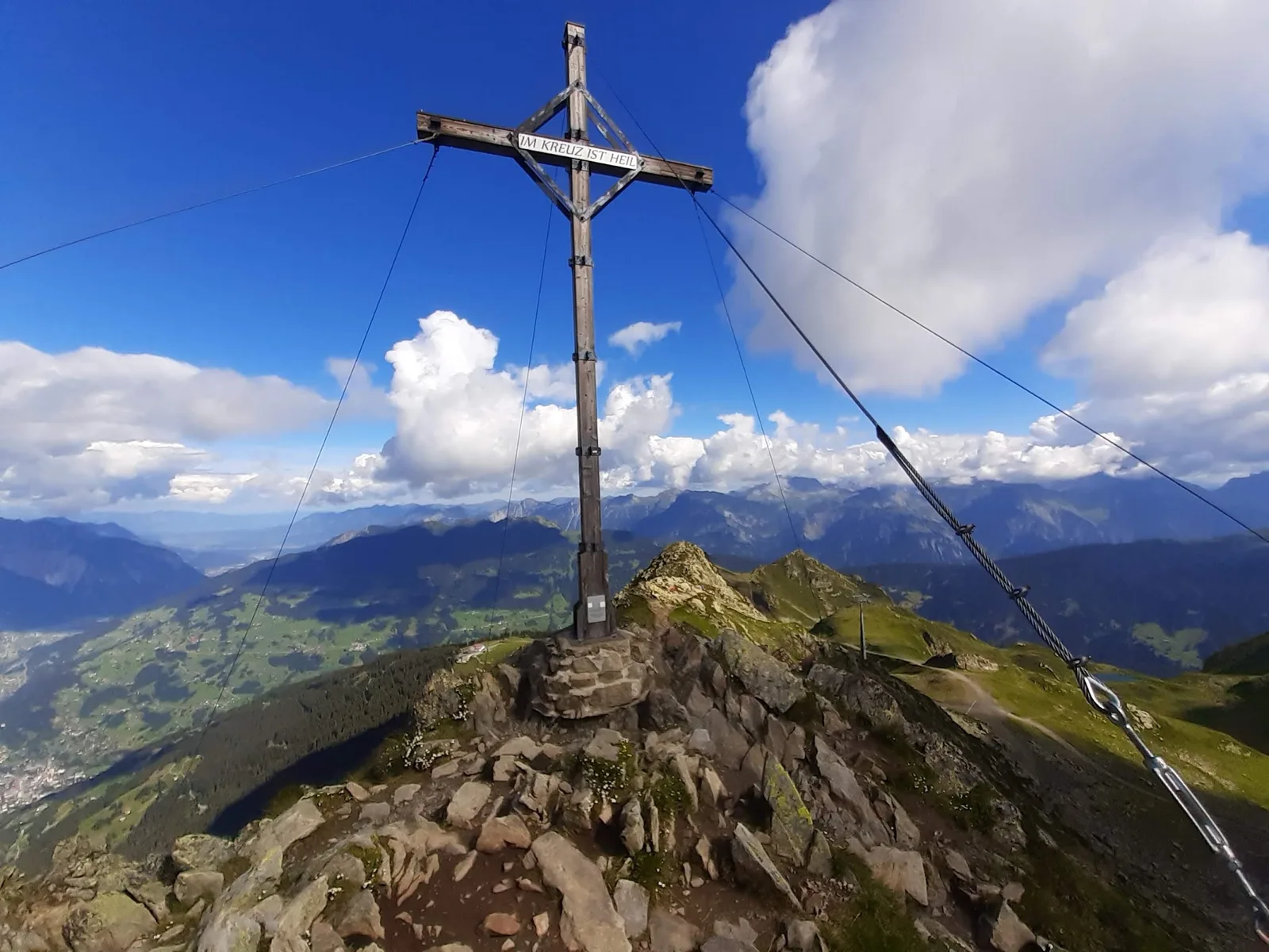 Ein Gipfelkreuz mit der Tafel Im Kreuz ist Heil, dahinter das Montafon