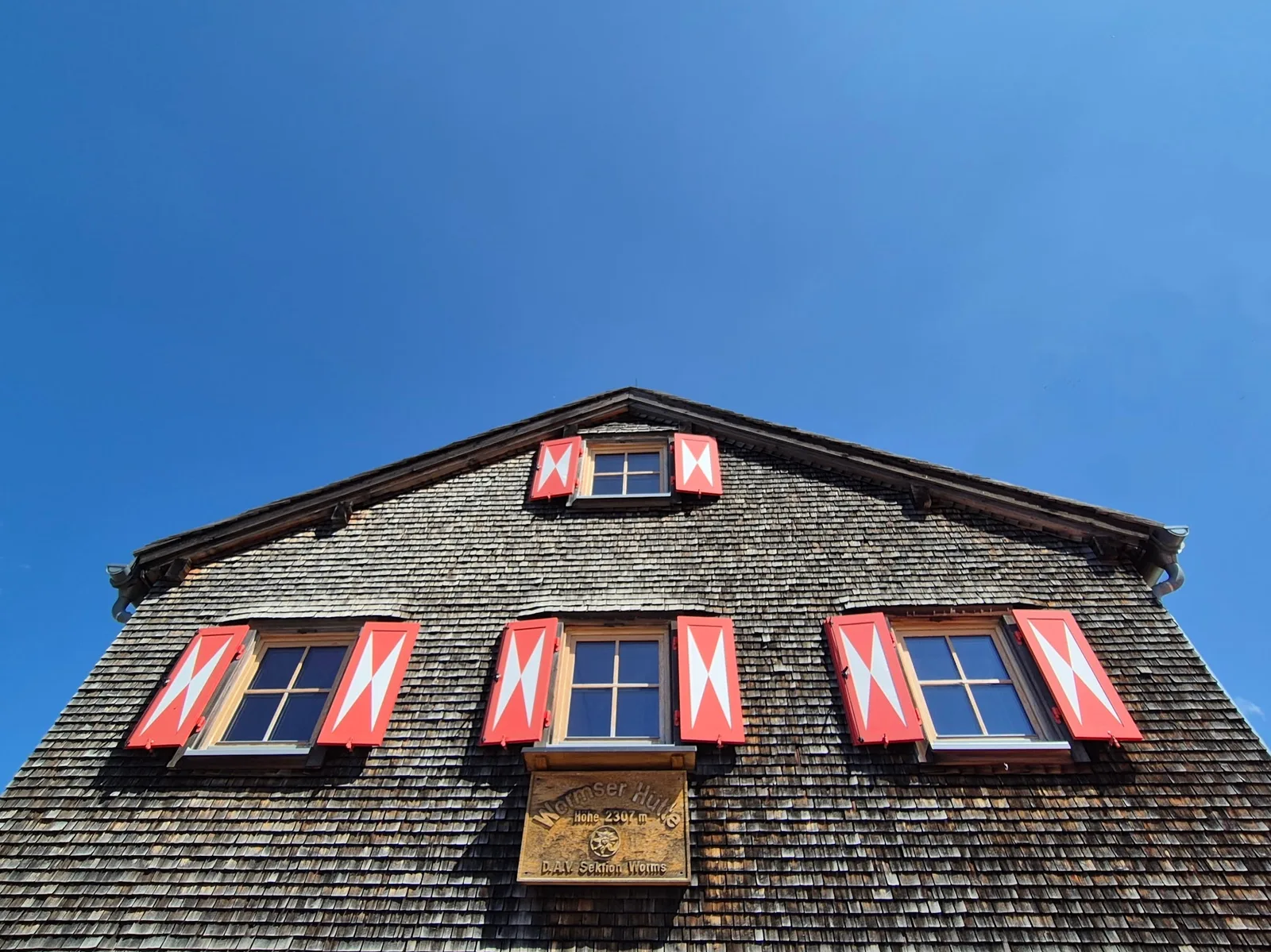Der Schindelgiebel der Wormser Hütte mit roten Fensterläden und dem geschnitzten Namensschild