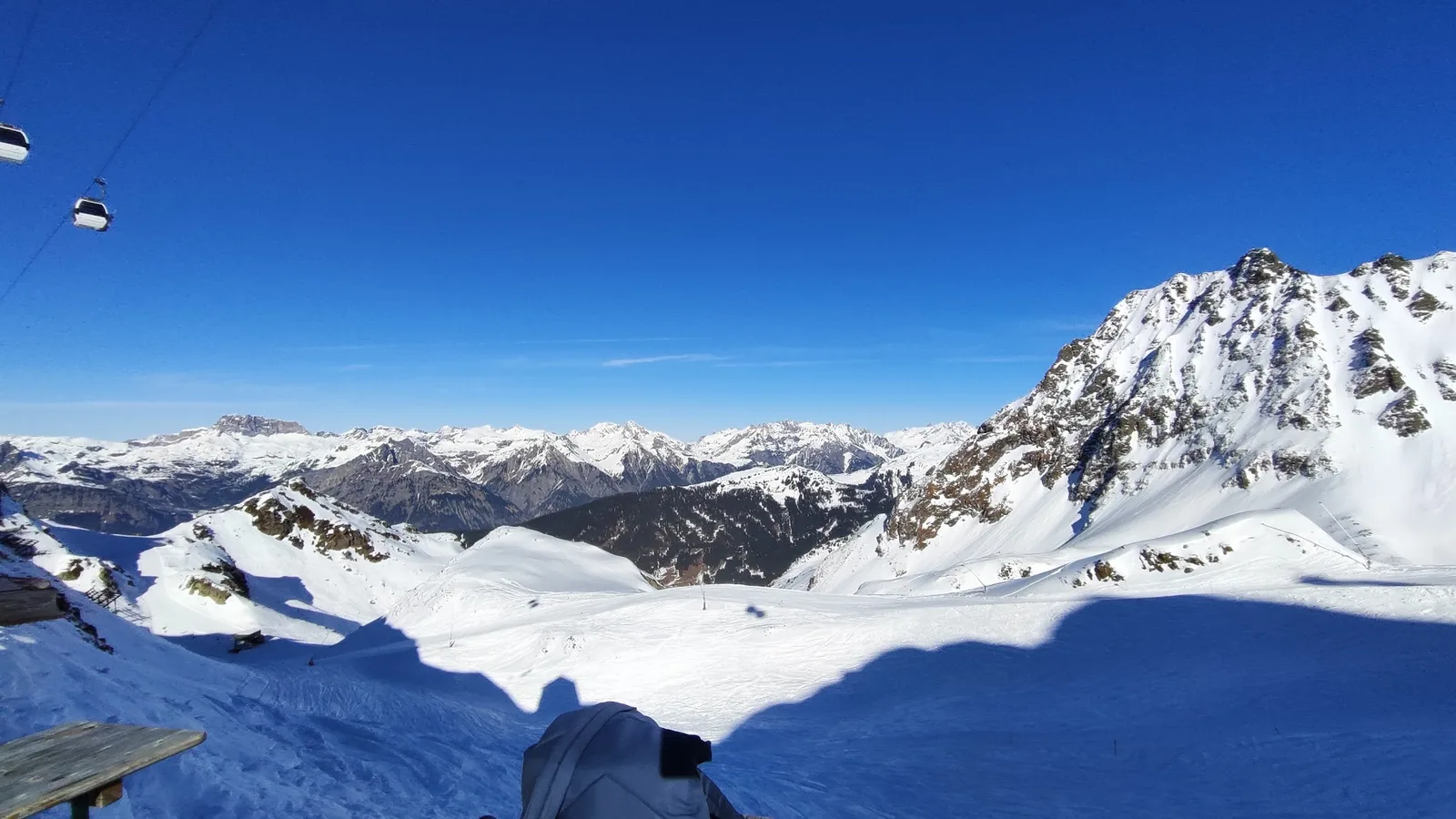 Winterpanorama von der Terrasse der Hütte, darüber Gondeln der Seilbahn