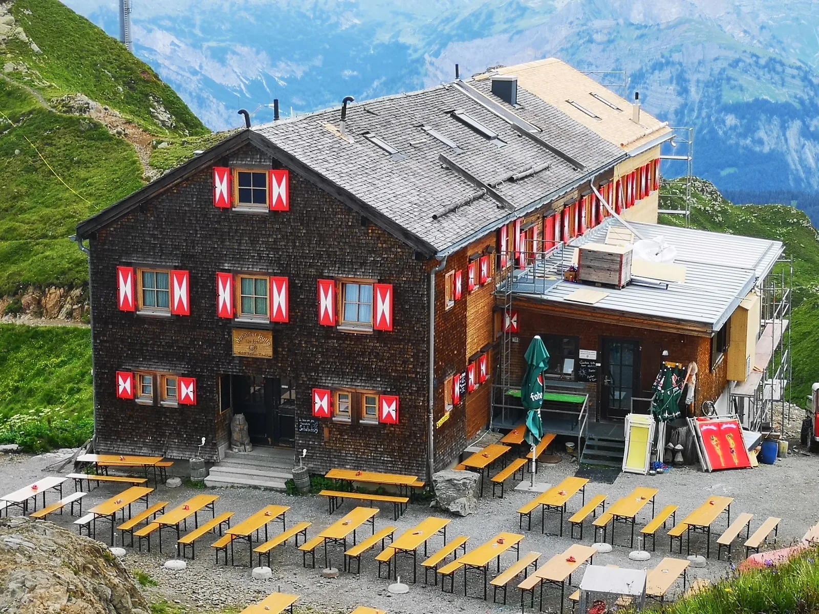 Die Wormser Hütte von oben, davor Reihen von Bierbänken auf dem Kies