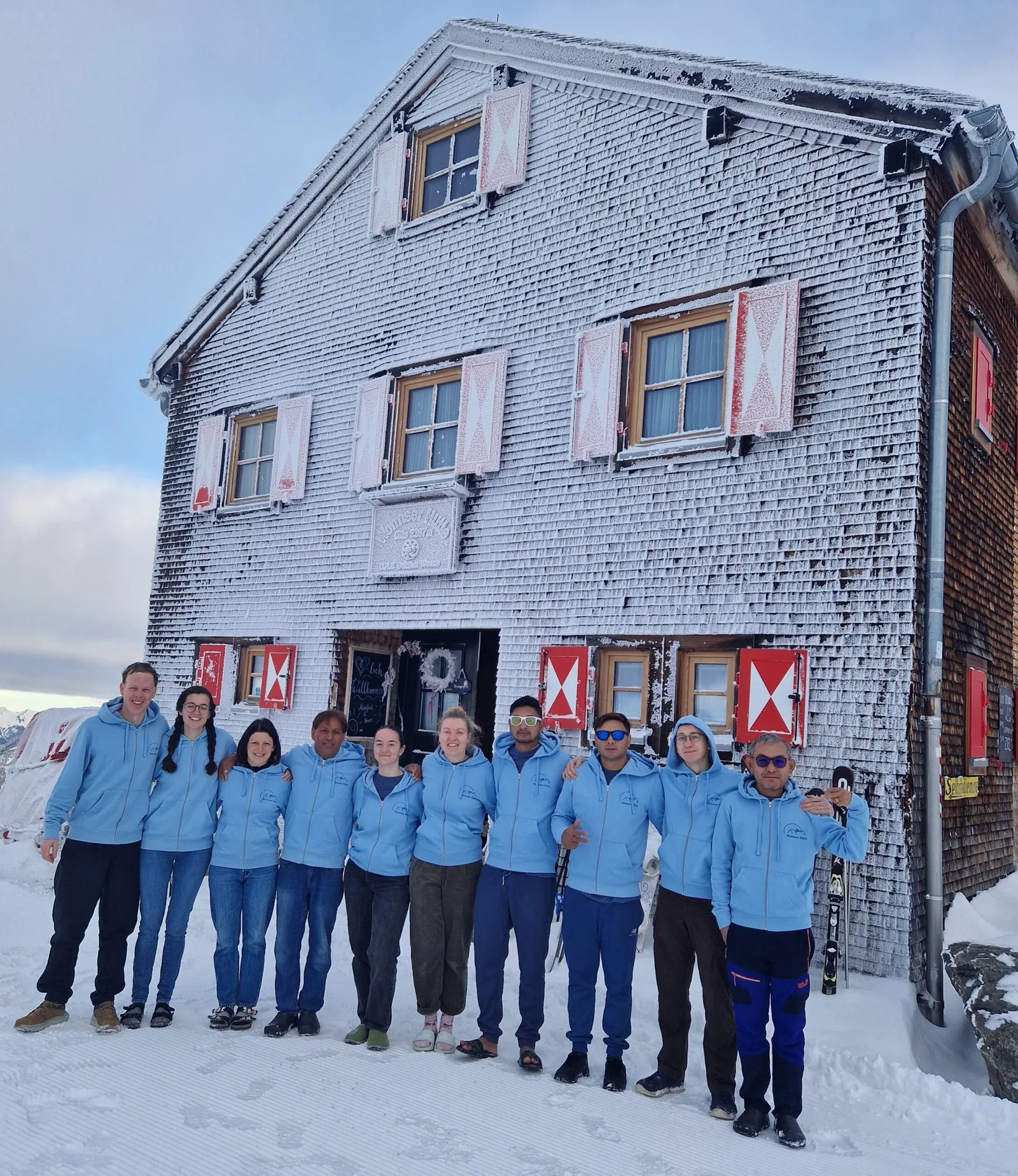 Elf Personen in hellblauen Hüttenpullis stehen vor der raureifbedeckten Wormser Hütte